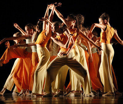 Eine Gruppe junger Tänzerinnen in orange- und beigefarbener Kleidung in unterschiedlichen Tanzpositionen. 