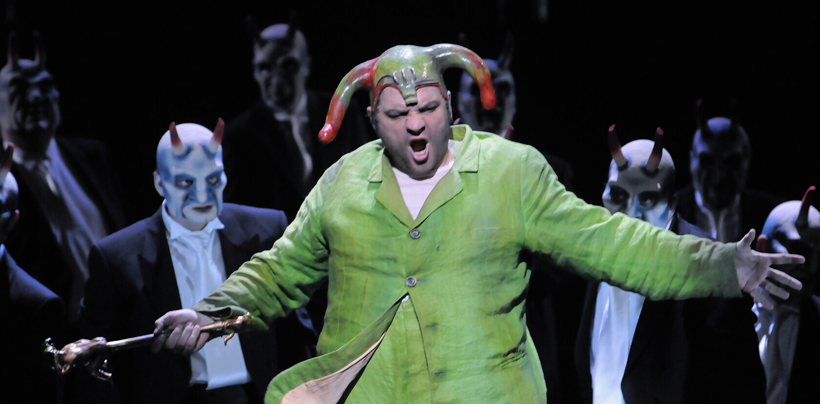 »Rigoletto« Szene aus "Rigoletto": Sänger in grünfarbenem Kostüm steht vor weiteren Sängern