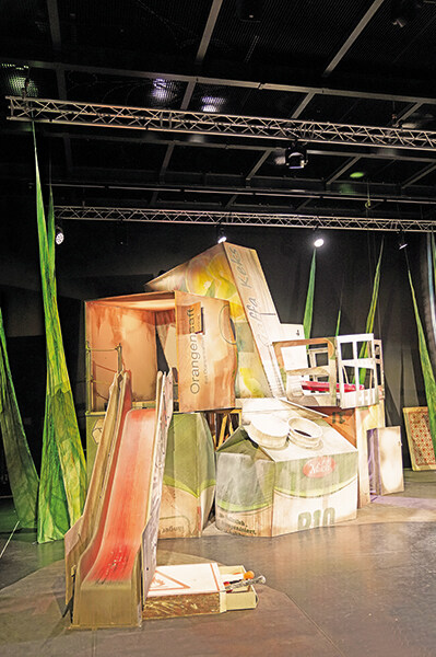 Bühnenbild von »Das schlaue Gretchen« bestehend aus übergroßen Saftkartons, Kekspackungen, einer Rutsche aus einer Zahnpasta-Packung und einer Streichholzschachtel mit Streichhölzern