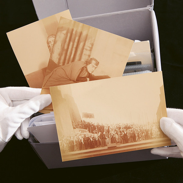 Zwei Hände mit weißen Handschuhen heben drei historische, sepia-farbene Fotografien aus einer Papp-Box