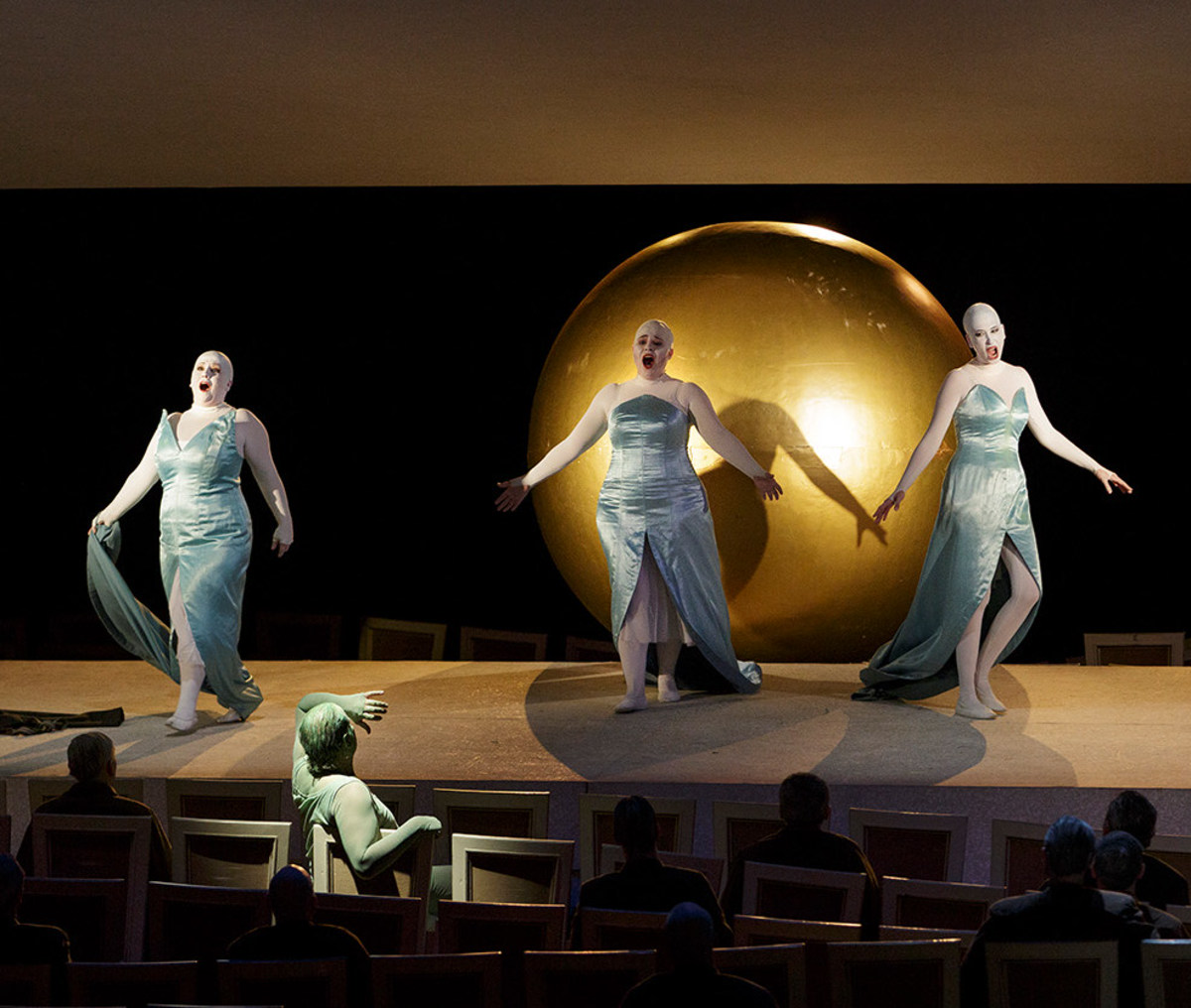 Szene aus "Das Rheingold": 3 Sängerinnen stehen vor großer goldfarbener Kugel