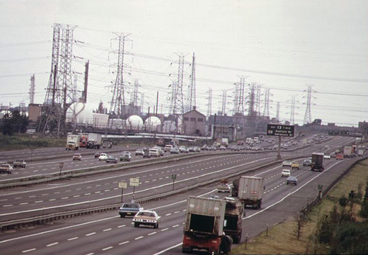New Jersey Turnpike, 1970: Im Vordergrund mehrere Straßen mit insgesamt zwölf Spuren und Standstreifen, im Hintergrund Industriebauten, zahlreiche Oberleitungen und Masten.