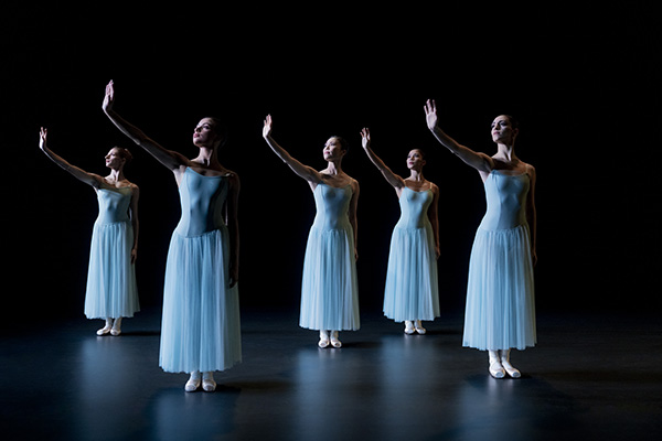 Fünf Ballett-Tänzerinnen stehen in weißen Kleidern auf der Bühne und haben den rechten Arm ausgestreckt.
